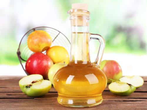 apple-cider-vinegar-in-glass-bottle-and-ripe-fresh-apples-on-wooden-table-on-nature-background